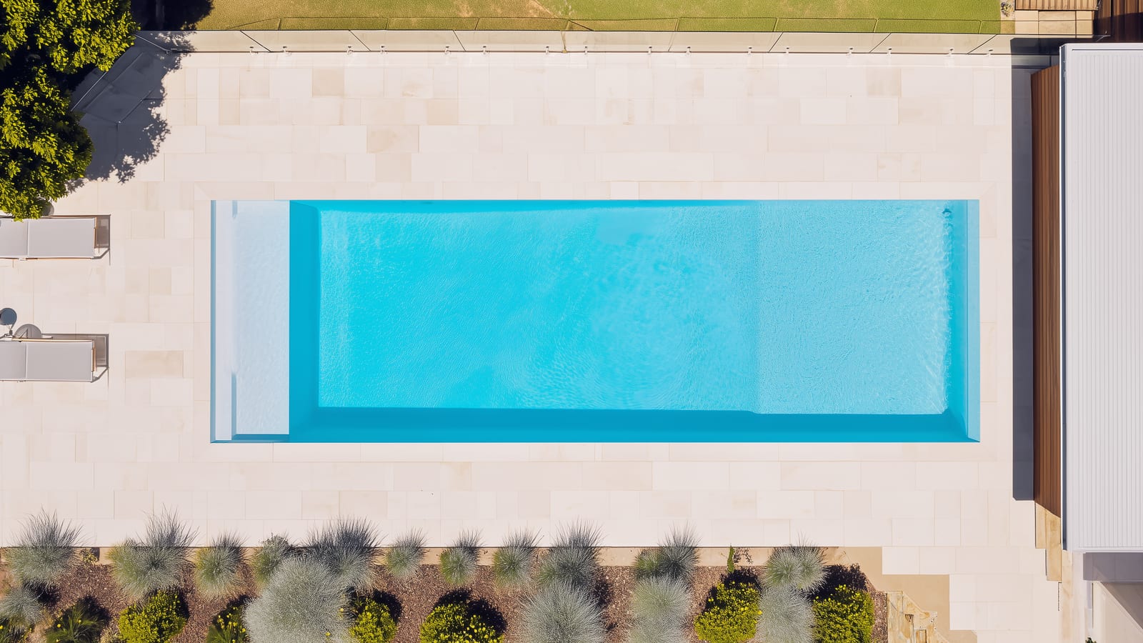 Top-down view of a rectangular backyard pool framed by pale paving and planting